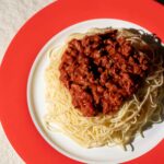 Plant-based spaghetti Bolognese with vegan mince in tomato sauce served on red Amoria-branded plate