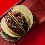Three plant-based beef tacos with lettuce, onion, and red chilies served on a red ceramic plate – Amoria Foods
