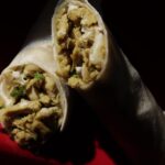 Sliced plant-based chicken shawarma wrap with golden vegan chicken, herbs, and garlic sauce on red background – Amoria Foods