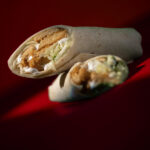 Sliced vegan chicken shawarma wrap with lettuce and garlic sauce on a red background – Amoria Foods