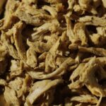 Close-up of Amoria plant-based chicken shreds showing fibrous texture and seasoning in a brass pan