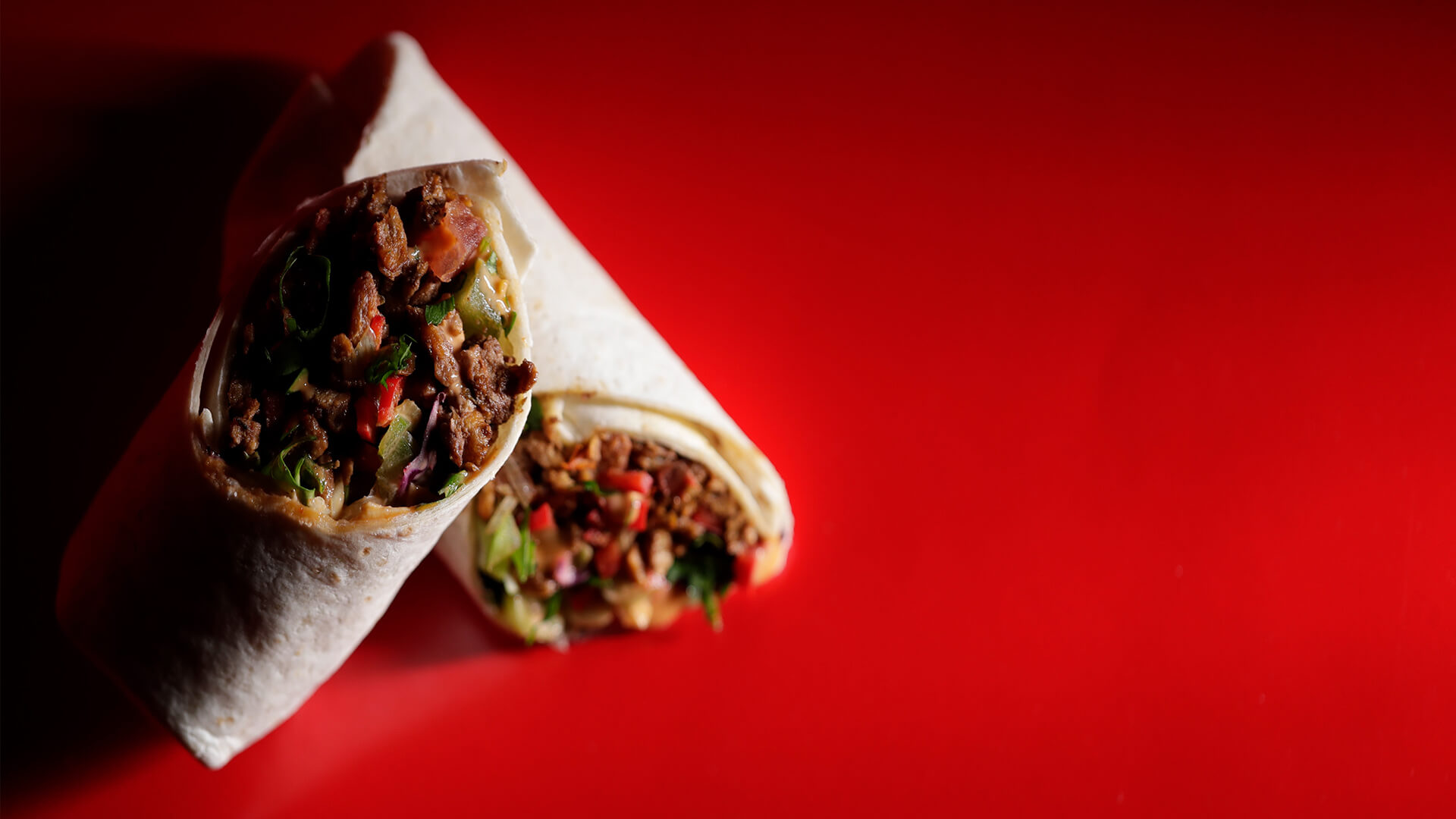 Plant-based vegan wrap filled with fresh vegetables and meat-free protein, placed on a vibrant red background.